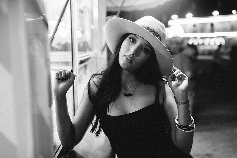 Black and white photo of a pretty young woman with a trendy outfit name necklace and hat on head