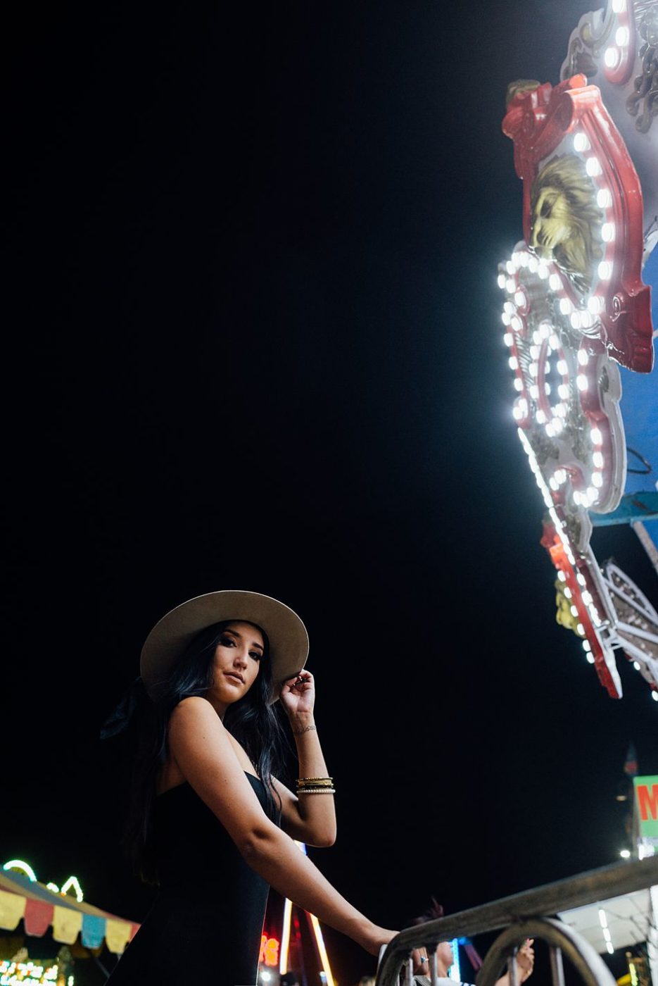 Pretty young woman in trendy clothes waiting in line by carnival ride lights 