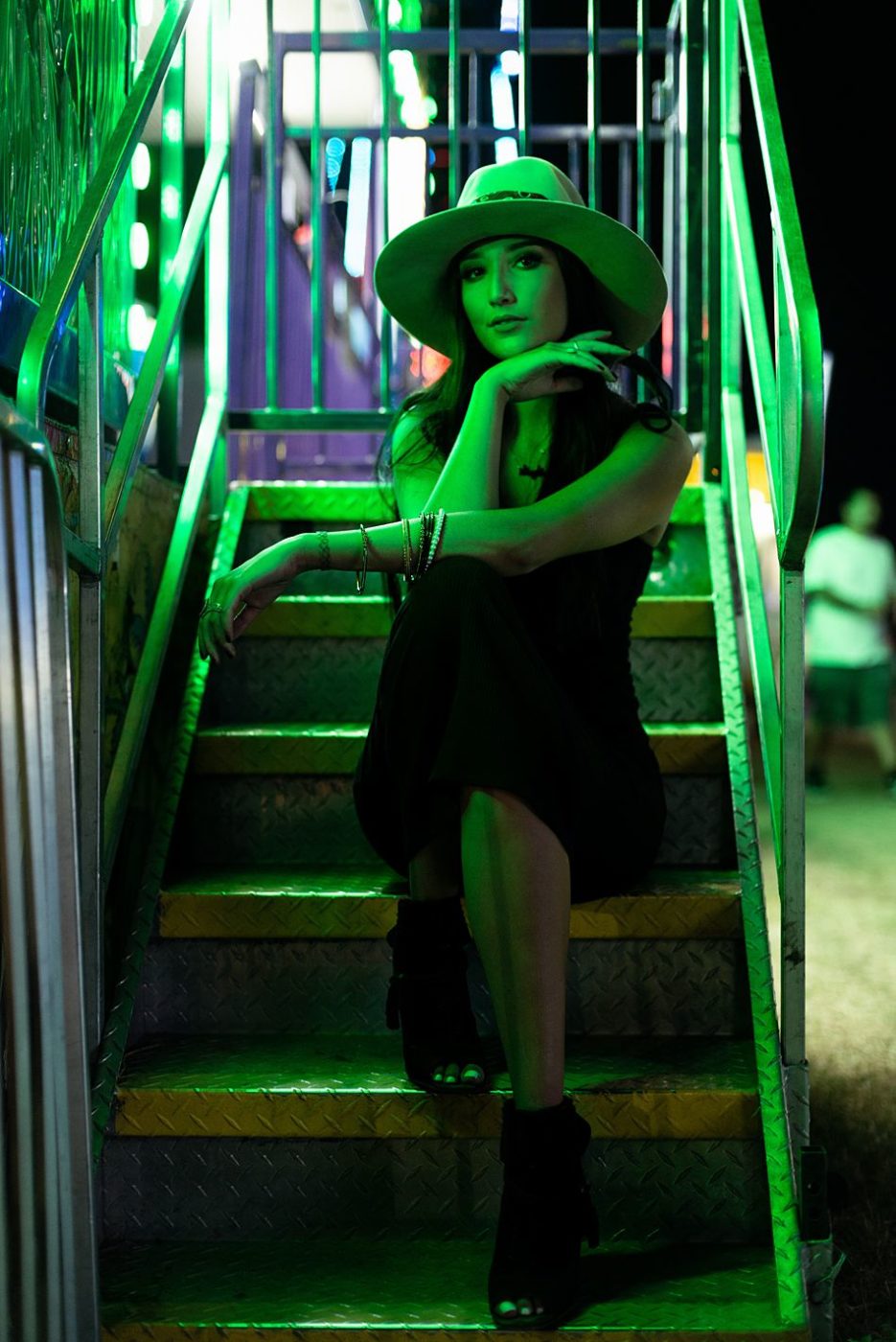 Pretty young woman sits on steps at the county fair in the green light of a carnival ride