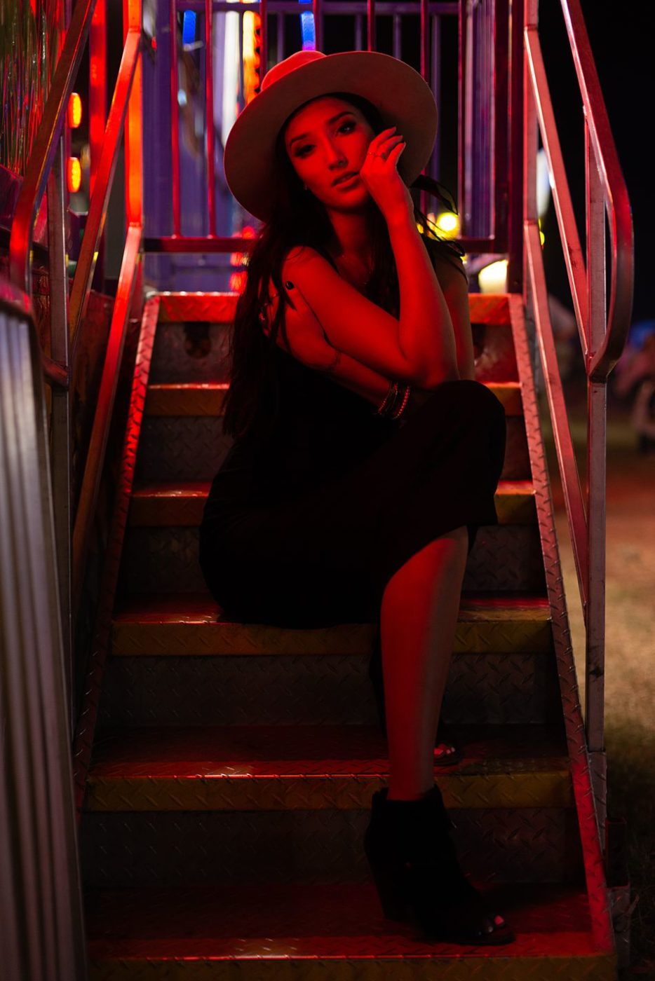 Pretty woman sits on steps at the county fair in the red light of a carnival ride