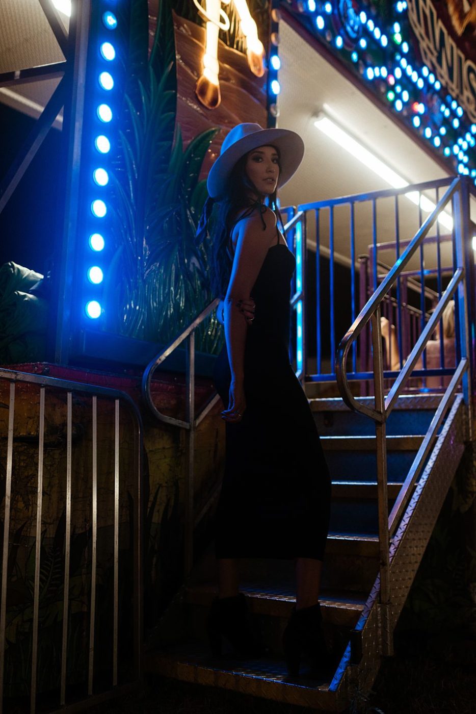 Pretty girl in trendy black dress and hat at carnival fair 