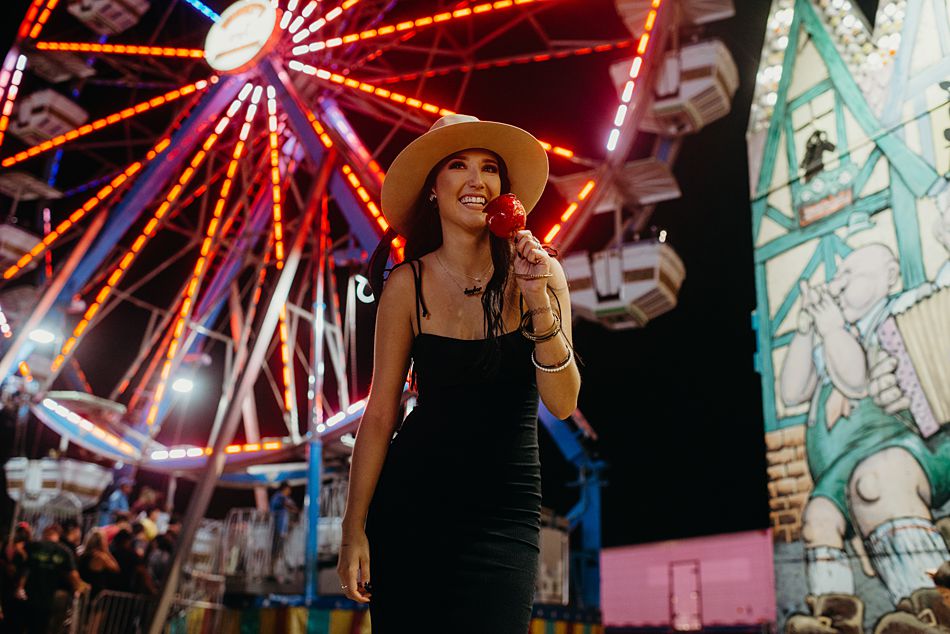 Pretty woman eating red candy apple in front of a ferris wheel
