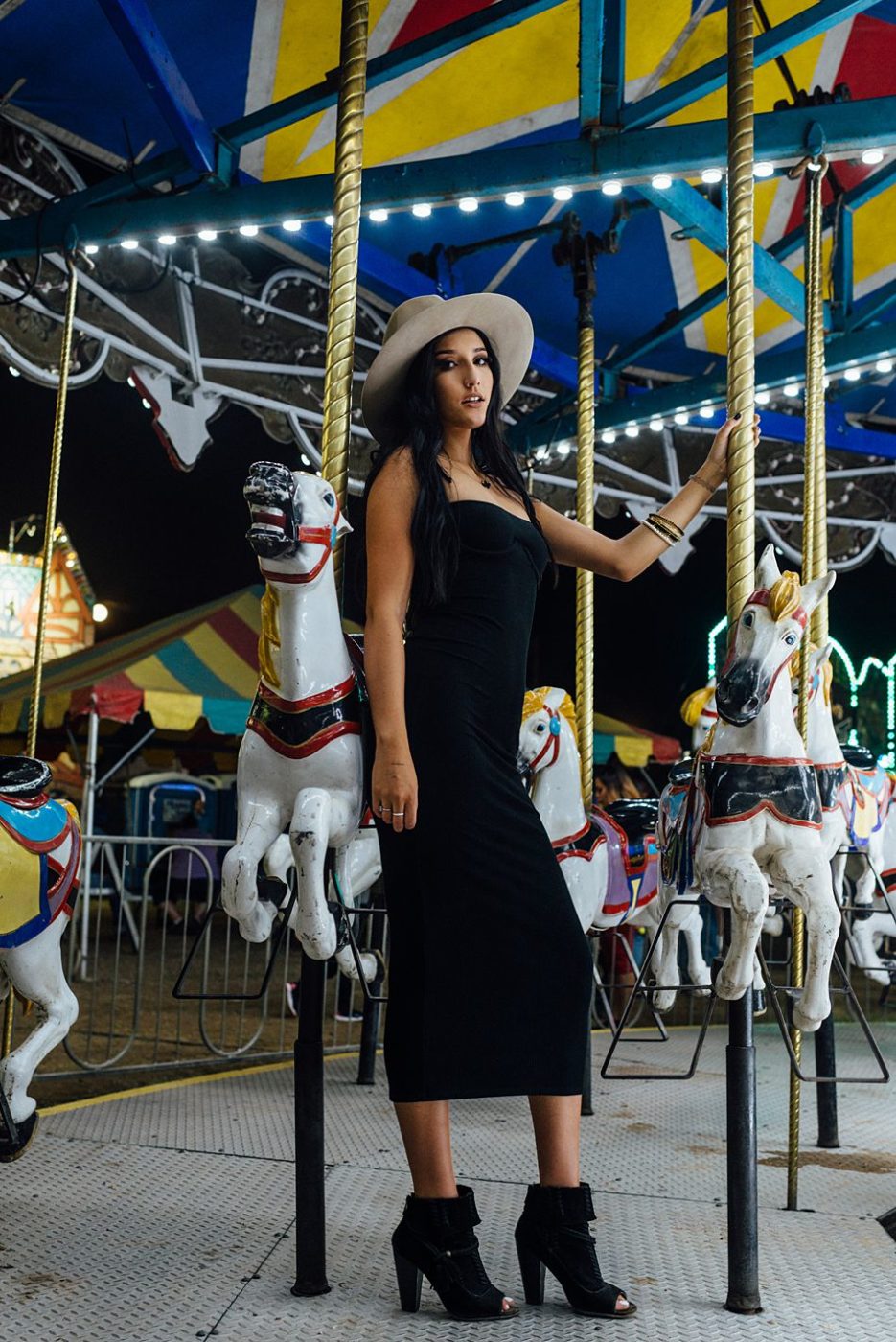 Pretty girl in black dress and hat on the carousel horse carnival ride