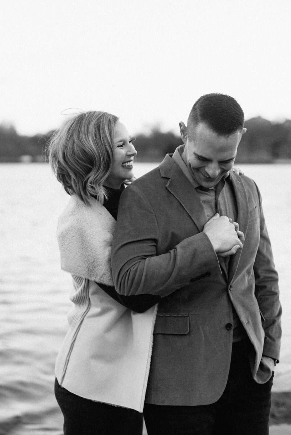 Black and white photo of a young couple smiles and laughs while embracing each other
